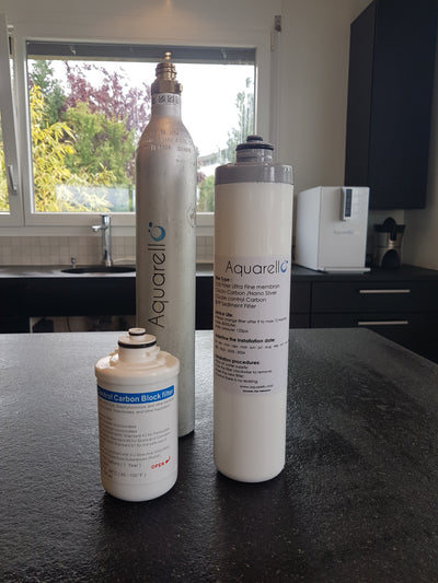 Bild zeigt alle drei Aquarello Zubehörprodukte – Wasserfilter, Gaskartuschen und Flaschen – für optimale Wasserspender-Qualität bei zuhause.